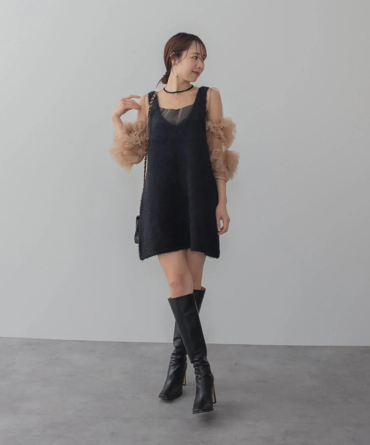 ベージュのチュール袖トップスに黒のミニ丈ニットワンピとロングブーツを合わせたIラインワンピースの着こなしスタイル。