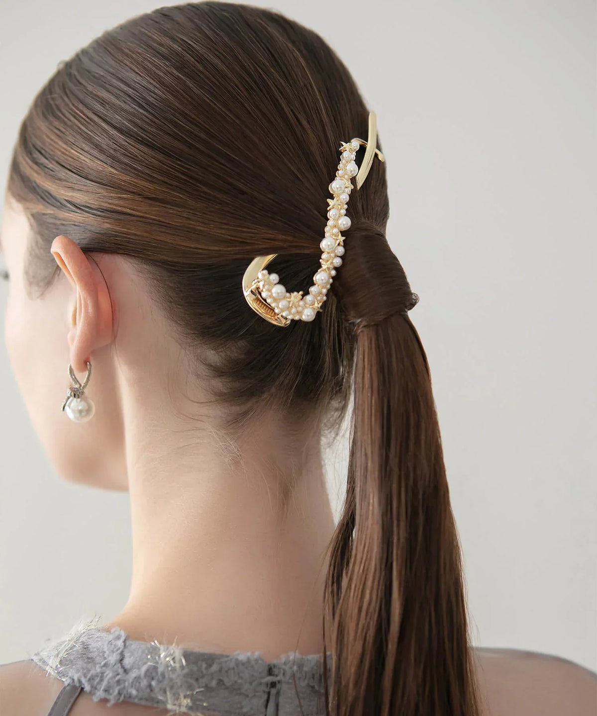 ポニーテールヘアの結び目に添えた、ゴールドのメタル曲線にパールと星モチーフをあしらったヘアクリップの後ろ姿。
