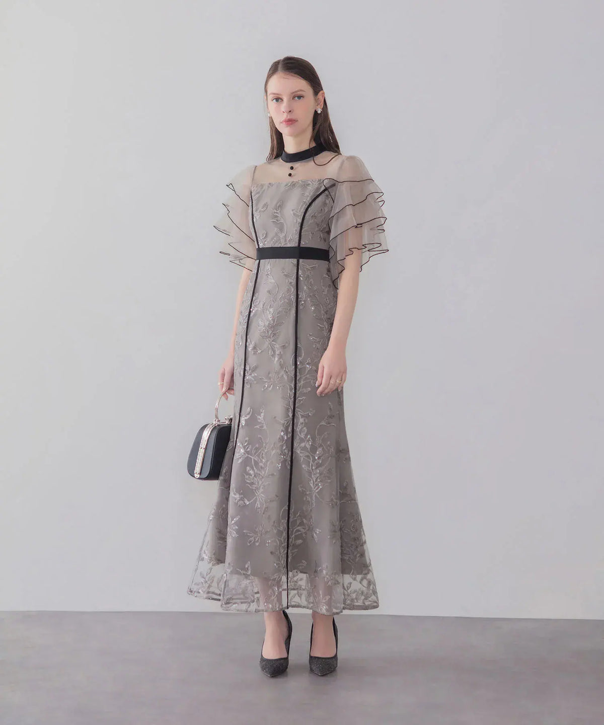 黒のパイピングとティアードフリル袖が華やかな、スパンコール刺繍入りグレーのマーメイドワンピースの全身スタイル