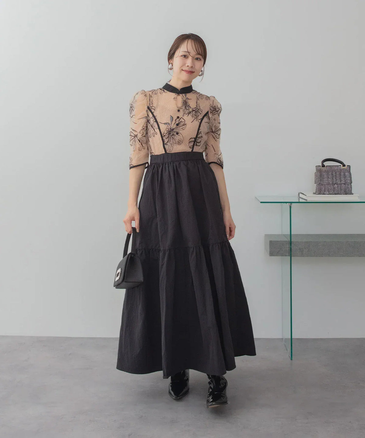 パイピングをあしらった花柄シフォンブラウスに黒のフレアスカートをドッキングしたロング丈のオケージョンドレスの全身スタイル。
