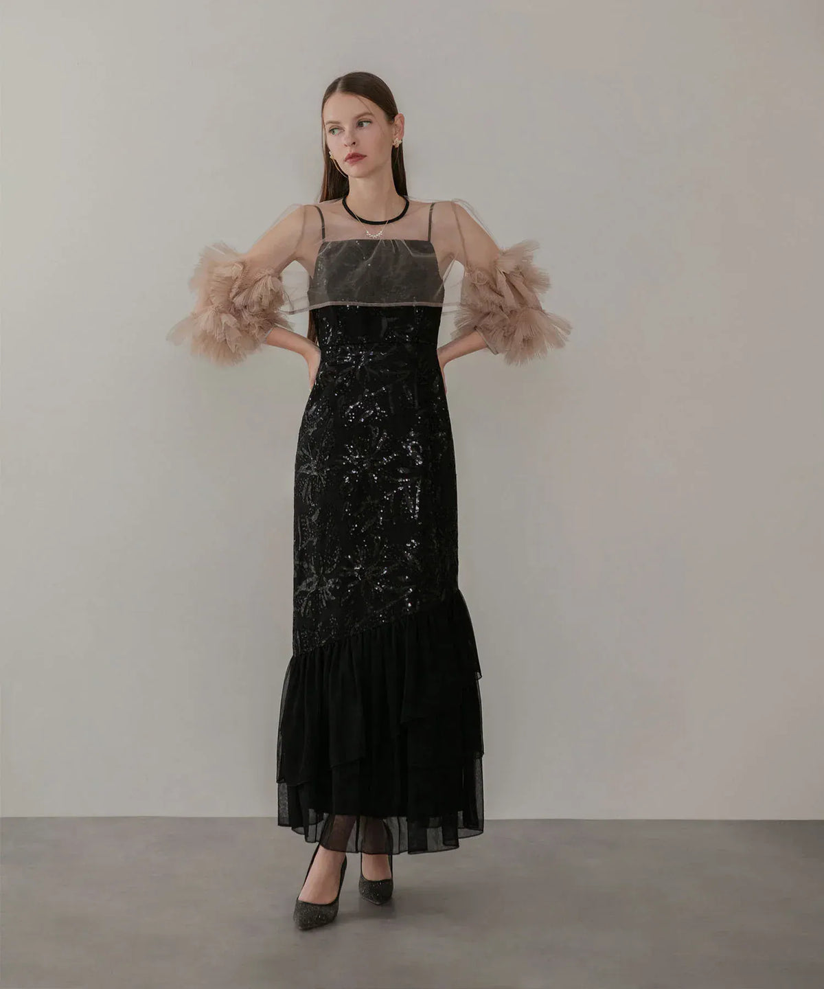 ベージュのフリルチュール袖ボレロを重ねた、黒のスパンコール刺繍と裾ティアードが映えるIラインオケージョンドレスの全身スタイル。