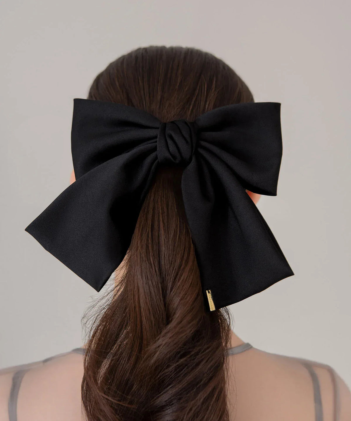 束ねた髪に黒のビッグリボンメタルプレートバレッタをつけた、上品で存在感のあるヘアアレンジの後ろ姿。