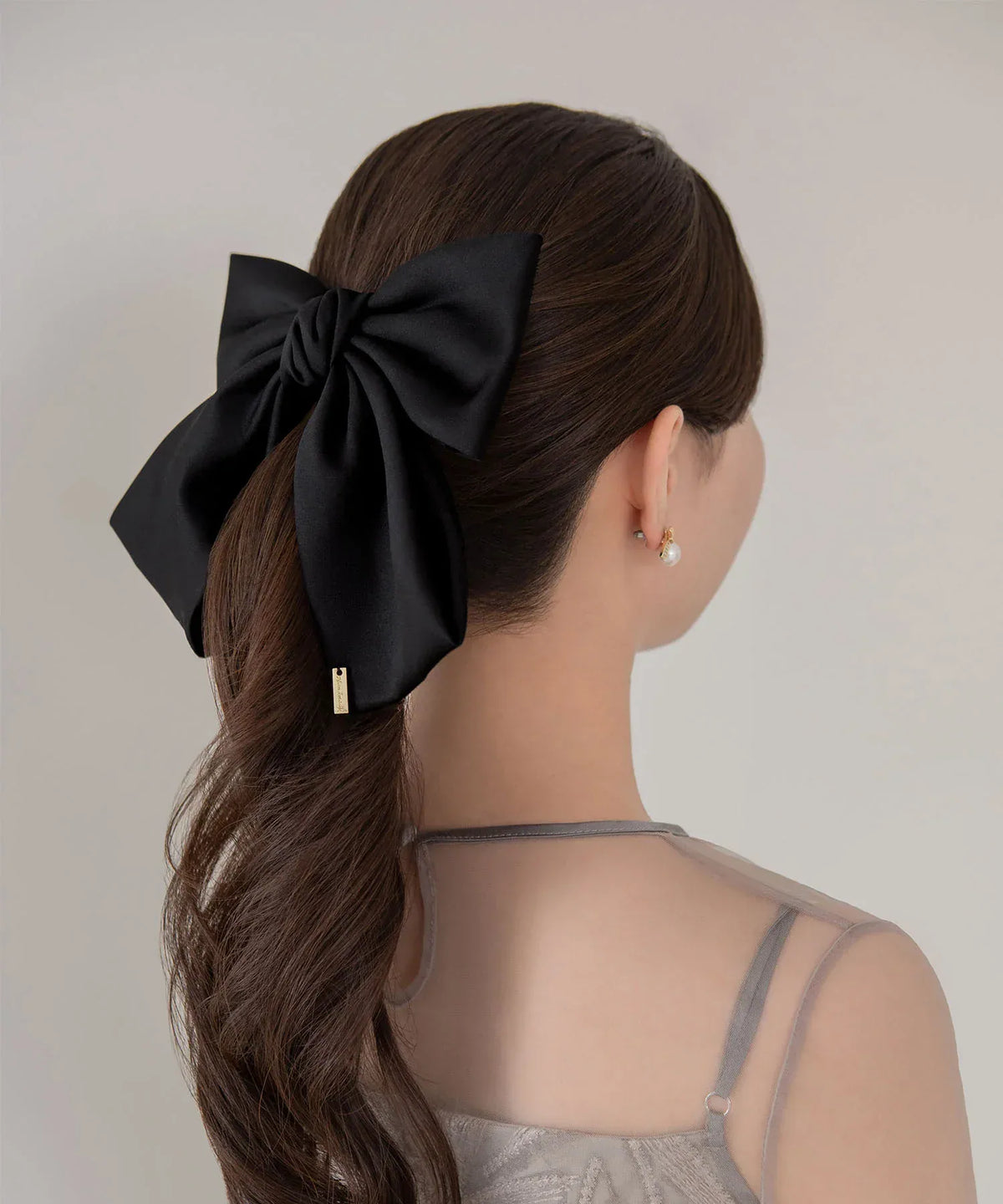 ポニーテールに黒のビッグリボンメタルプレートバレッタを留めた、上品なヘアアレンジの後ろ姿。