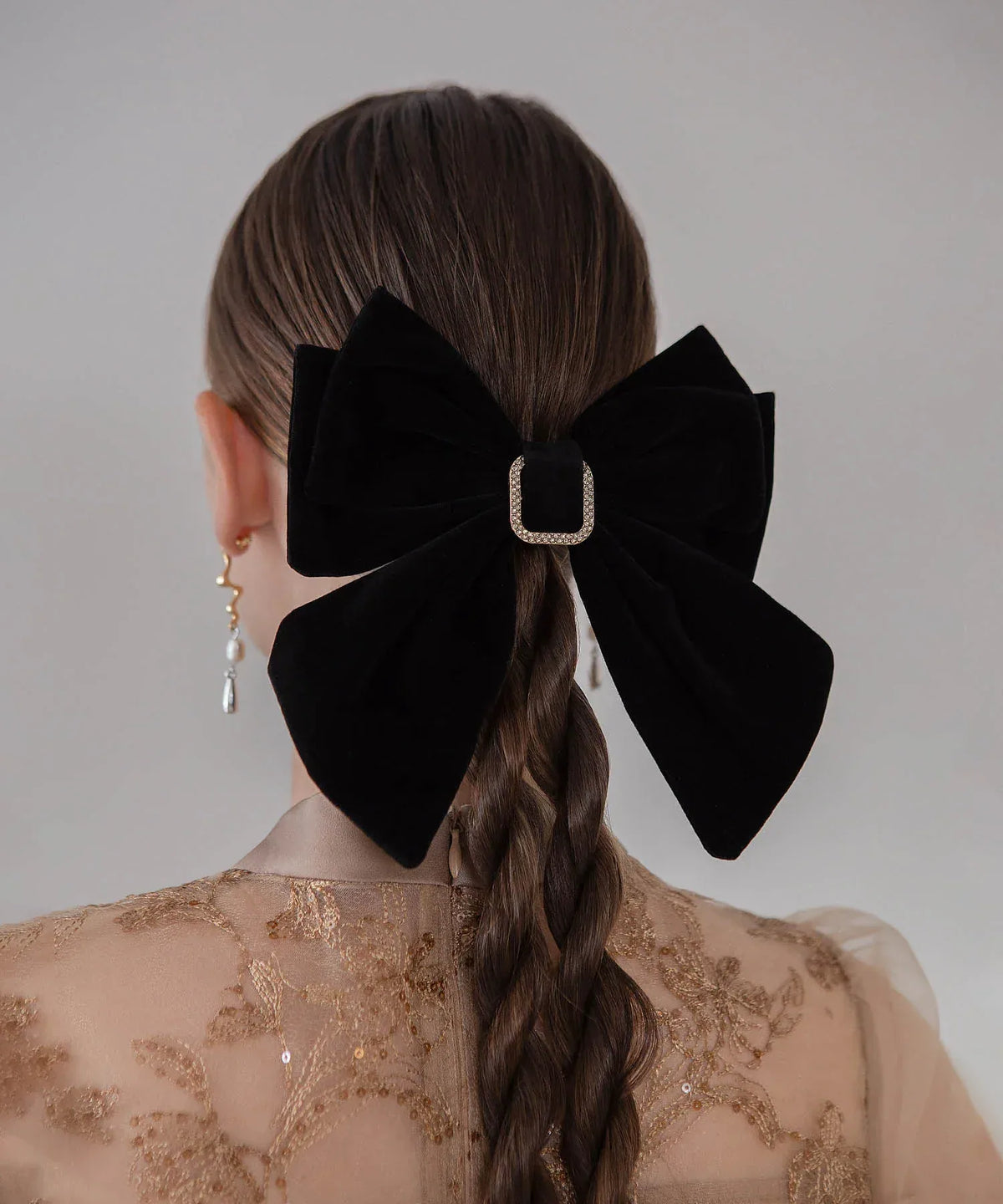 スクエアビジューバックルが輝く黒のベロアビッグリボンバレッタを、編み込みヘアに留めた華やかな後ろ姿。
