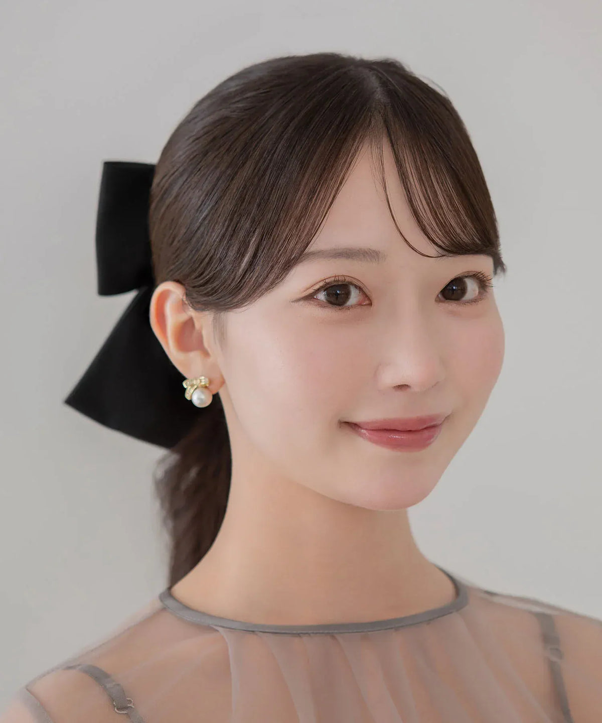 まとめ髪の女性のサイドから見えるブラックのビッグリボンメタルプレートバレッタが、シアーなオケージョンドレスと上品に調和する着用スタイル。