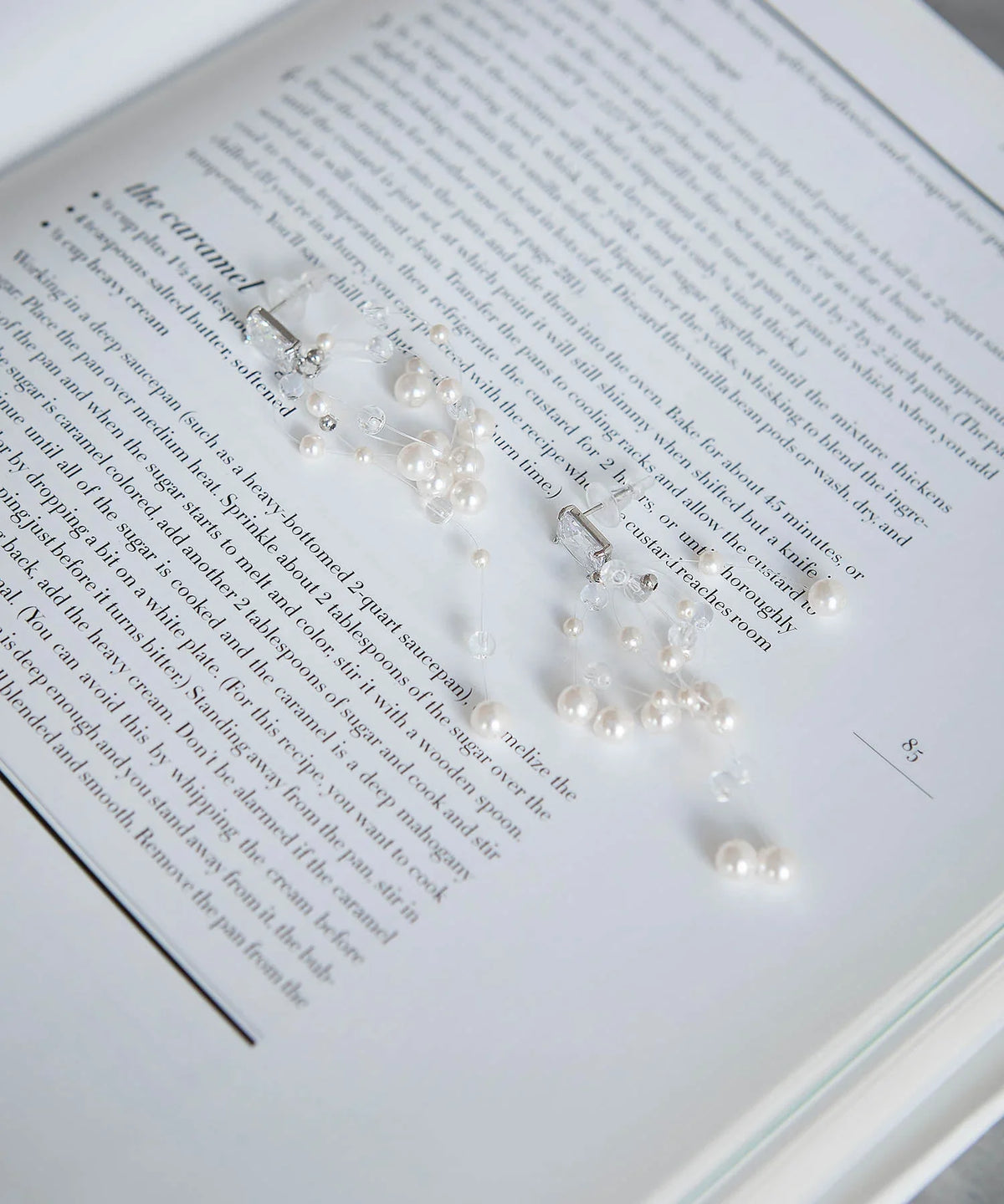 洋書の上に置かれた、スクエアビジューに繊細なワイヤーと小粒パールビーズが揺れるデザインが特徴のパールクリアビーズワイヤーモチーフピアス。