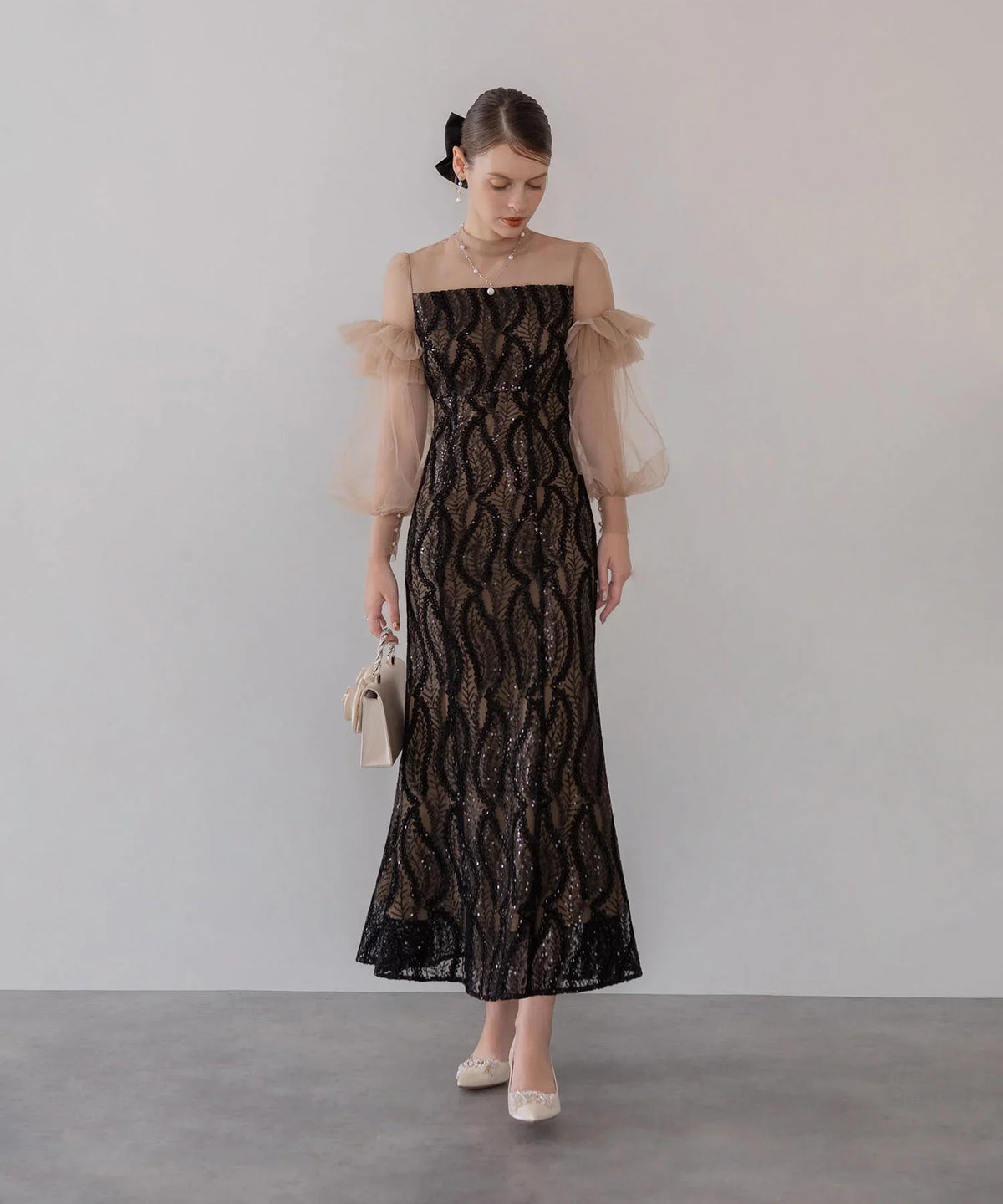 ベージュのシアーチュール袖と黒のリーフ柄スパンコール刺繍が華やかな、結婚式にも映えるマーメイドワンピースの全身立ち姿。
