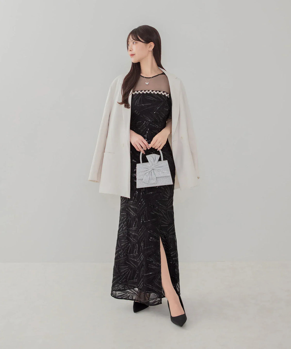 黒のロングドレスと白ジャケットに合わせた、シルバーのグリッタービッグリボン2WAYパーティーバッグの手持ちスタイル。
