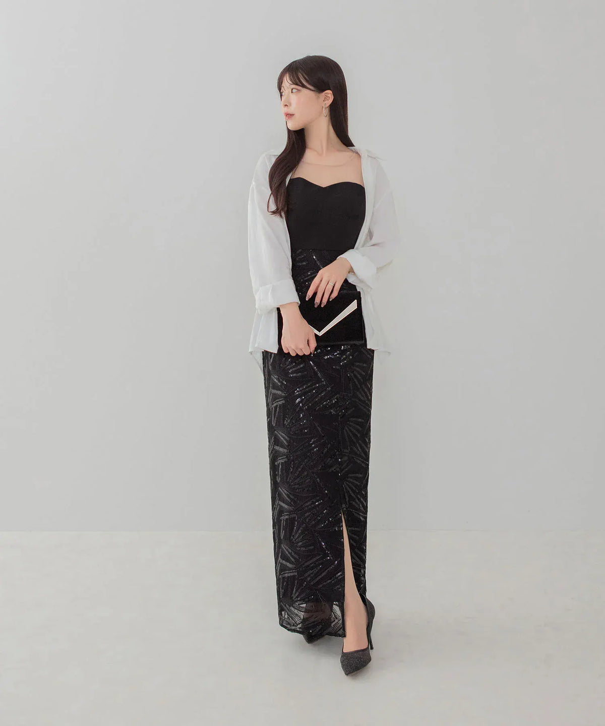 黒のビスチェ風ロングドレスに白シャツを羽織り、手元に添えたVカットメタルパーツが輝く黒のベロアクラッチバッグのコーディネート例。