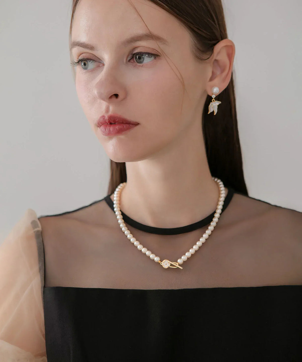 黒いシアー切替ドレスを着た女性が着用する、上品な小粒ホワイトパールとゴールドの花モチーフ留め具が華やかなエレガントフラワーパールネックレス。