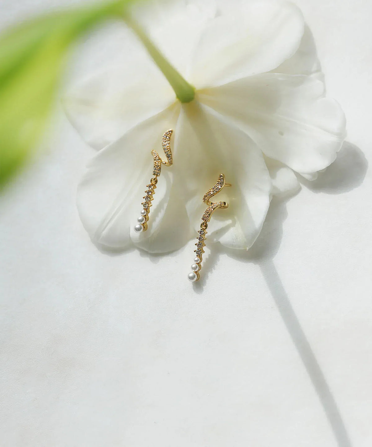 白い花びらの上に置かれた、ビジューと小粒パールが輝くゴールドのツイストバーピアス。結婚式やパーティーにも映える繊細で華やかな揺れるデザイン。