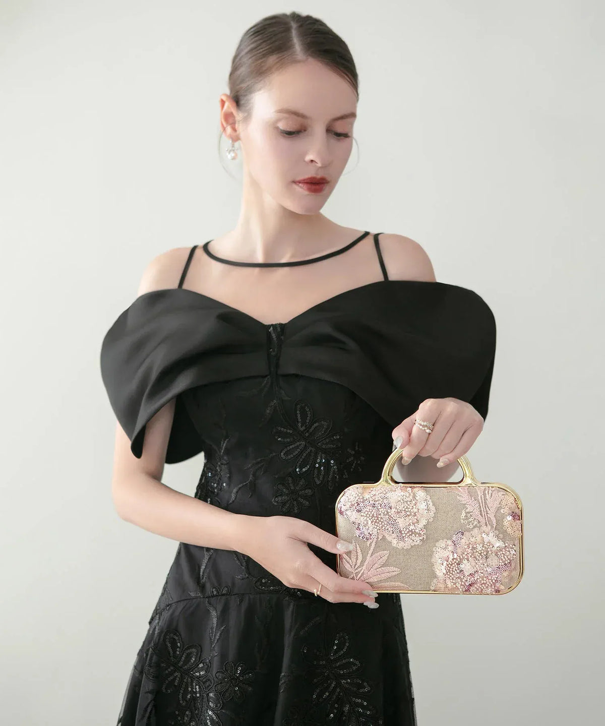 黒のパーティードレスを着た女性が手元に持つ、華やかなフラワー刺繍とスパンコールビーズが施されたゴールドフレームの2WAYバッグ。