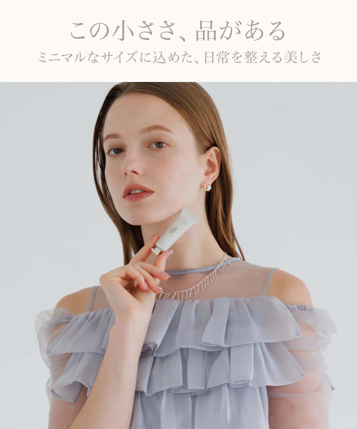 首元に掲げた手のひらサイズの白いチューブでコンパクトなサイズ感が伝わるミニハンドクリーム。