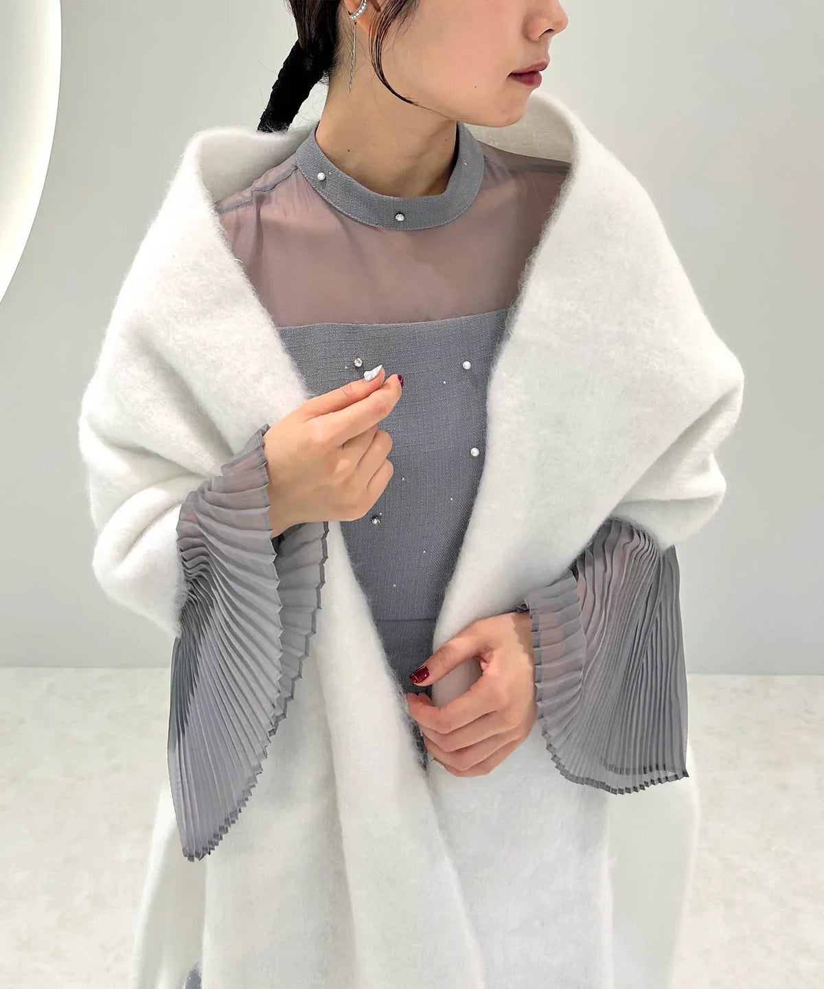 グレーのシースルードレスの上にふんわりと羽織った、起毛感のある白のシンプルフリンジマフラーのショール風アレンジ。