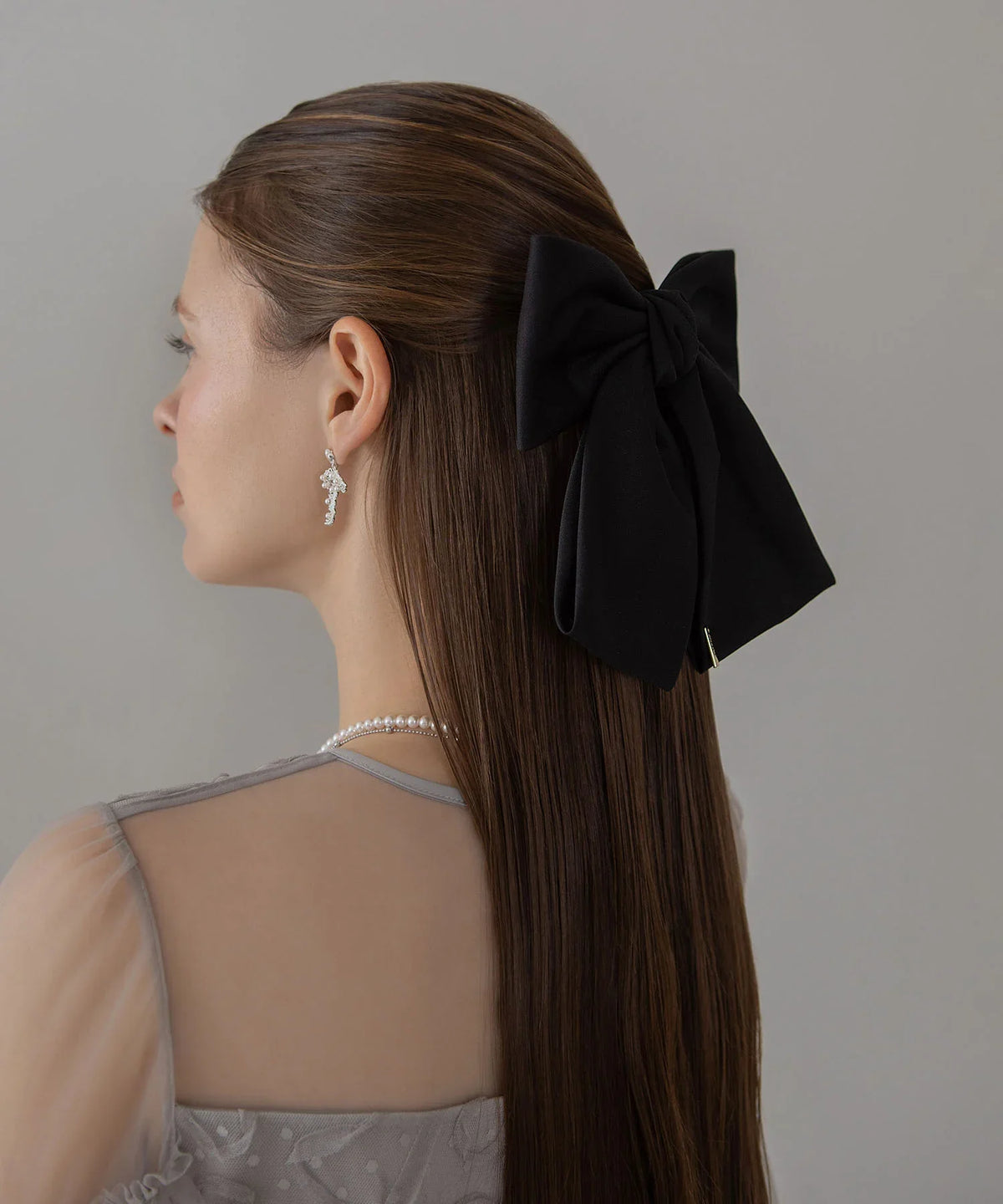 ハーフアップのロングヘアに黒のビッグリボンメタルプレートバレッタを留めた、上品な後ろ姿の着用コーディネート。