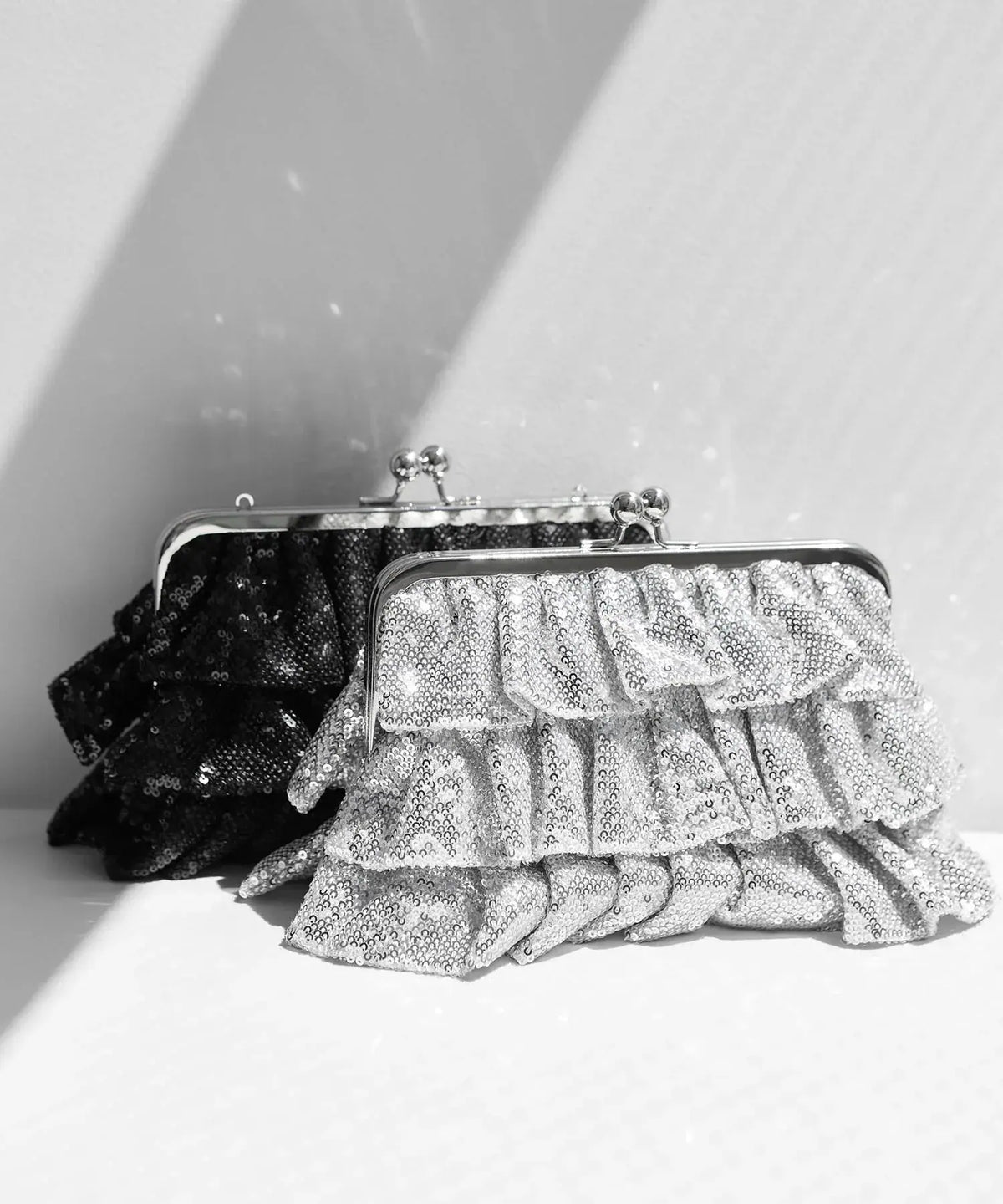 きらめくスパンコールの段フリルとシルバーのがま口金具が華やかな、シルバーとブラックのクラッチバッグ。
