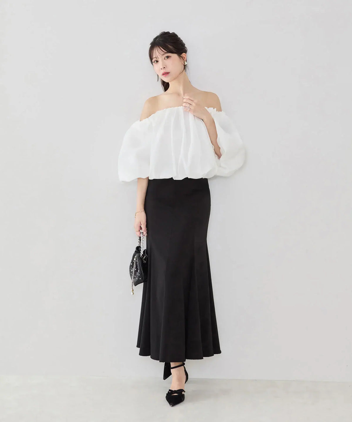 黒のロングマーメイドスカートに合わせた、ふんわりとした白のバルーンオフショルトップスの全身コーディネート。
